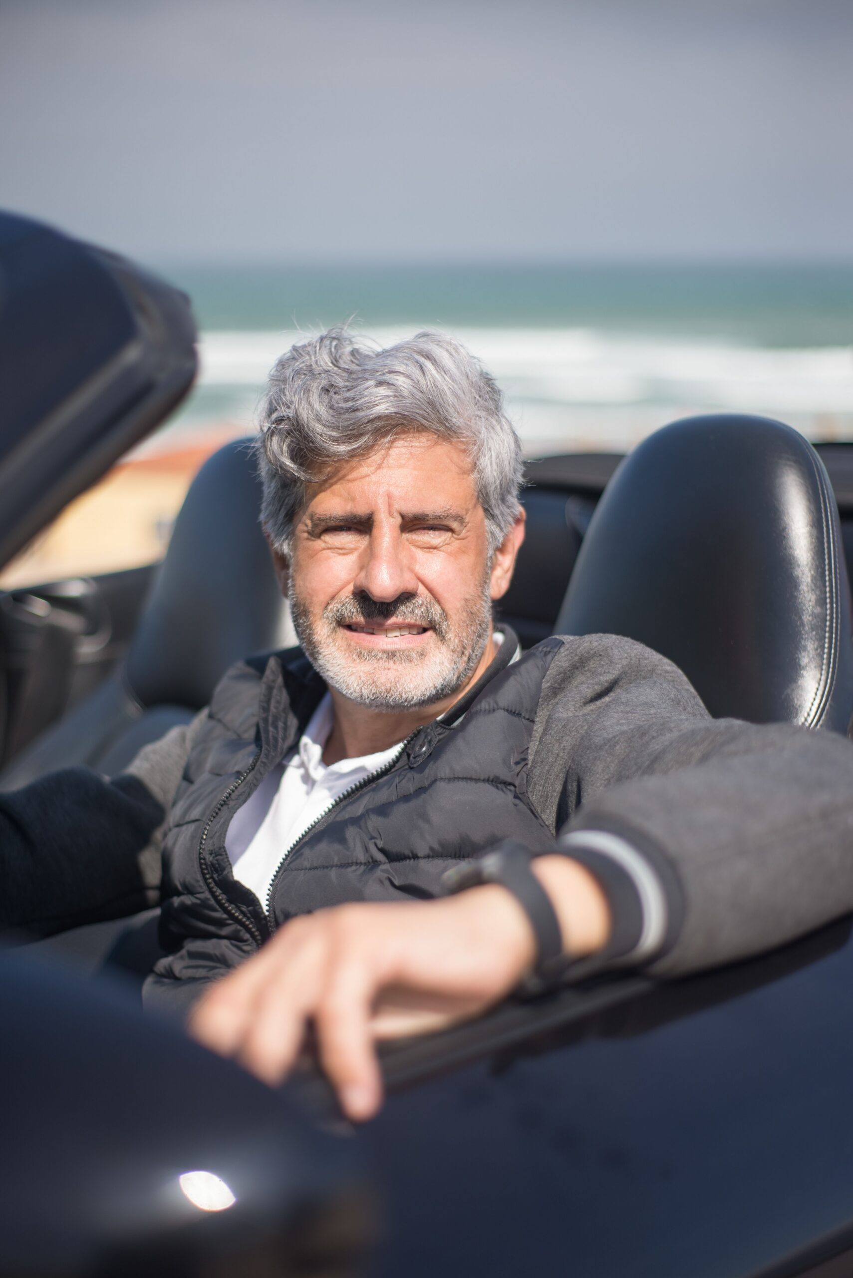 Senior man with gray hair driving a convertible by the ocean, enjoying a sunny day.